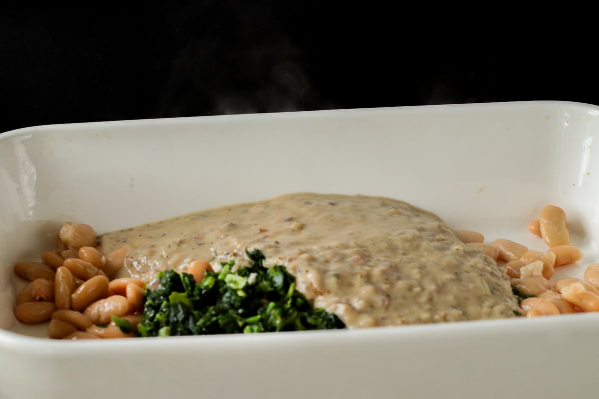 adding white sauce to the spinach and white beans in the casserole dish
