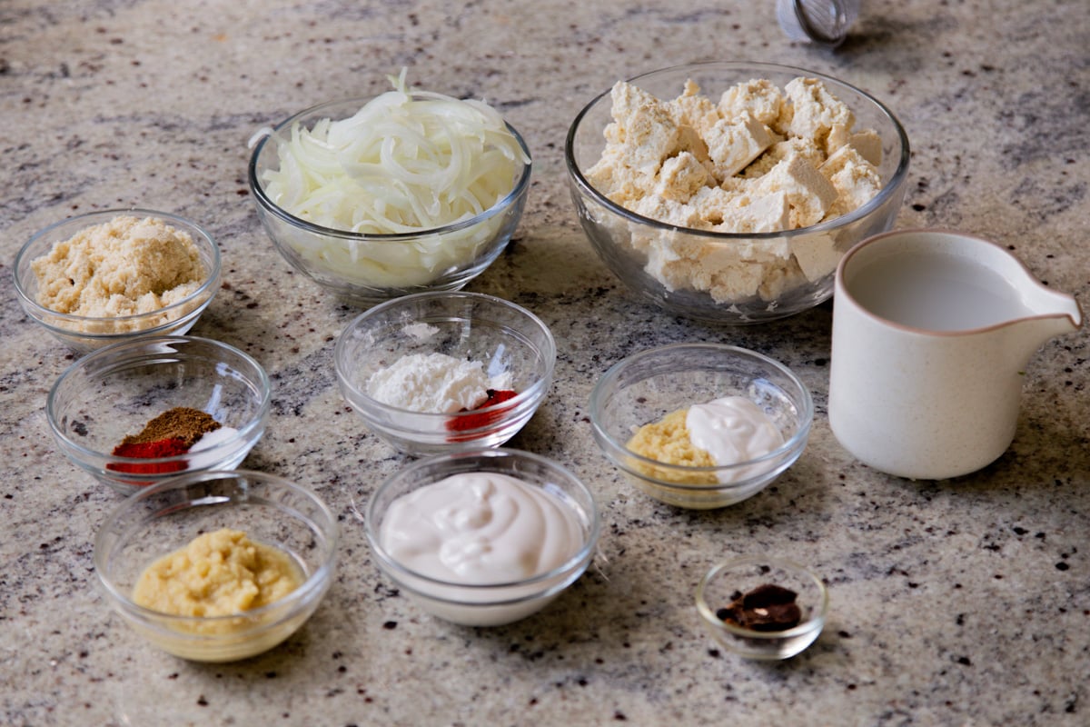 tofu, onions, spices, and other curry ingredients in bowls on a kitchen counter